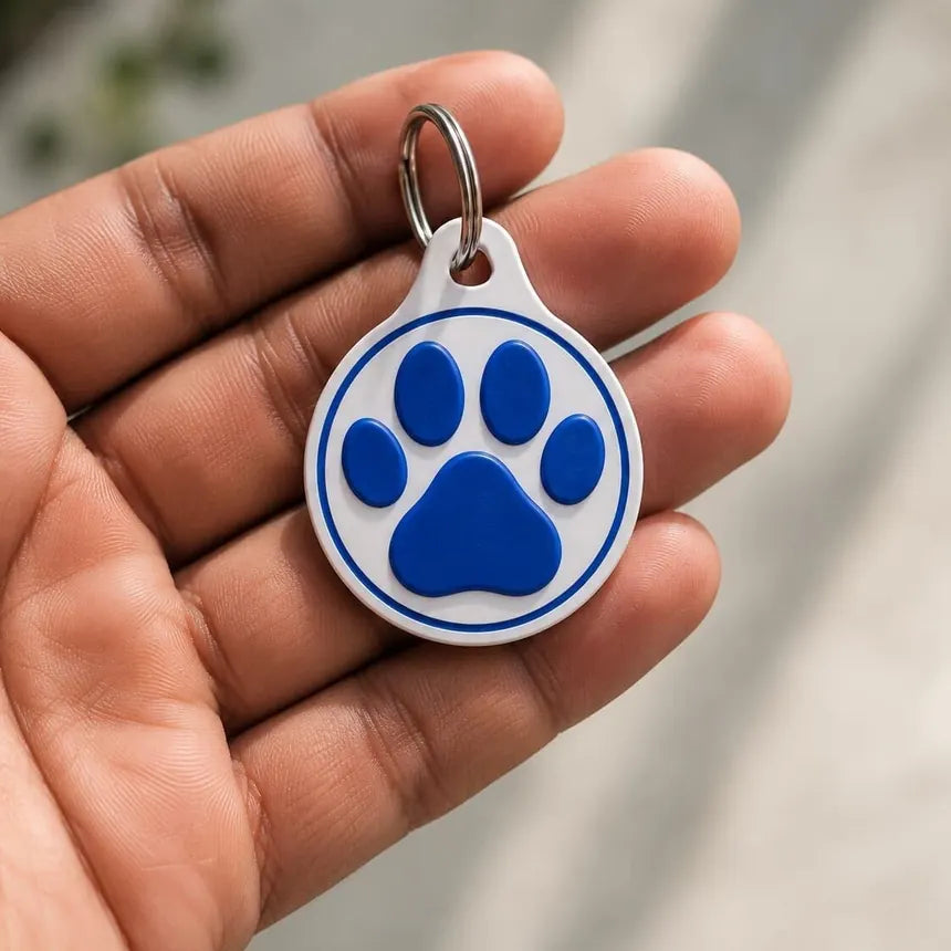The front of the VitalPaws One Tag Gen 5 in a hand: a round white tag with a blue paw