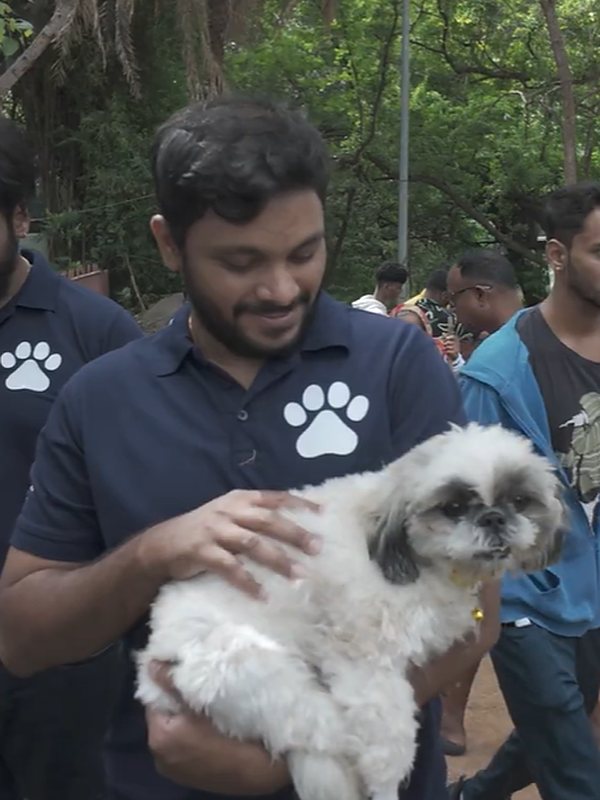 A Vital Paws team member in a paw-print T-shirt holding a small white dog at the Reunite tag event