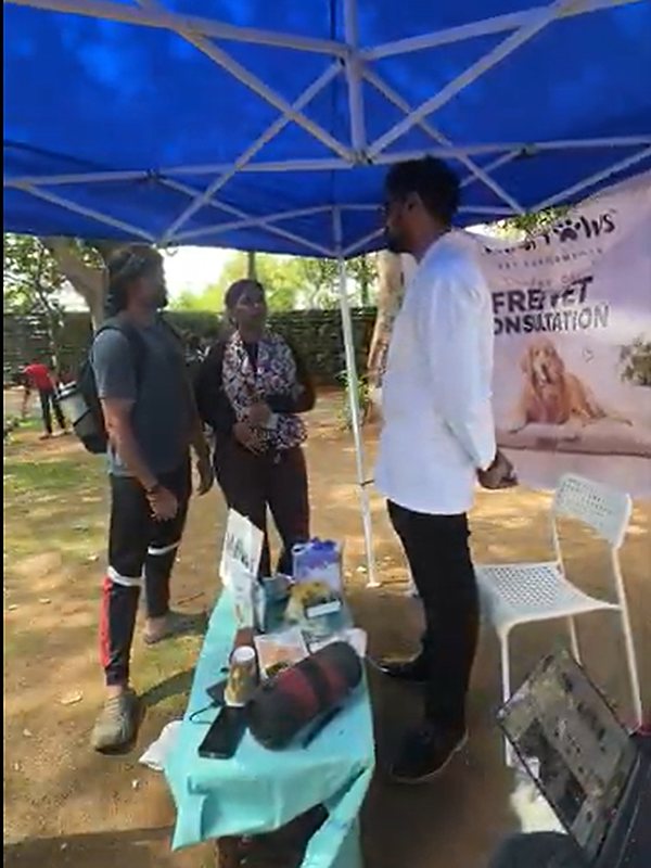 A vet in a white coat talking with two dog parents under the Vital Paws free vet consultation tent